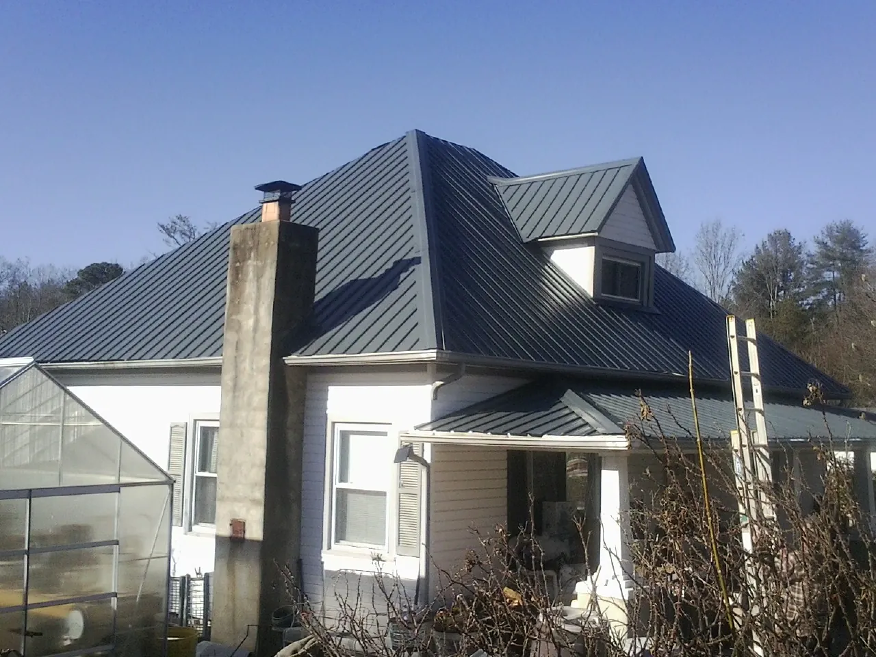 Dark blue standing seam metal roof on a white farmhouse with dormer — Slate & Tile Roof Repair by Roofing Brothers in North Ridgeville