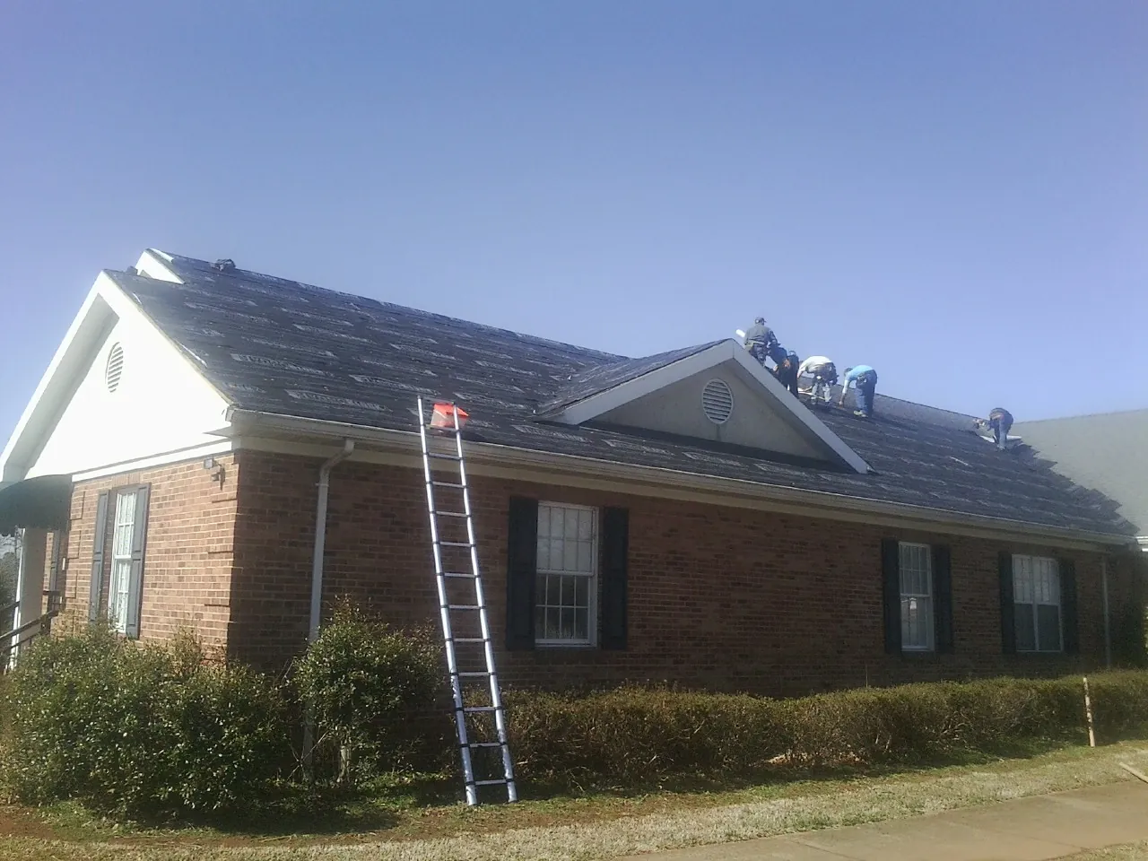 Crew tearing shingles off a brick ranch roof with a ladder set — Emergency Roof Repair work by our crew in North Ridgeville