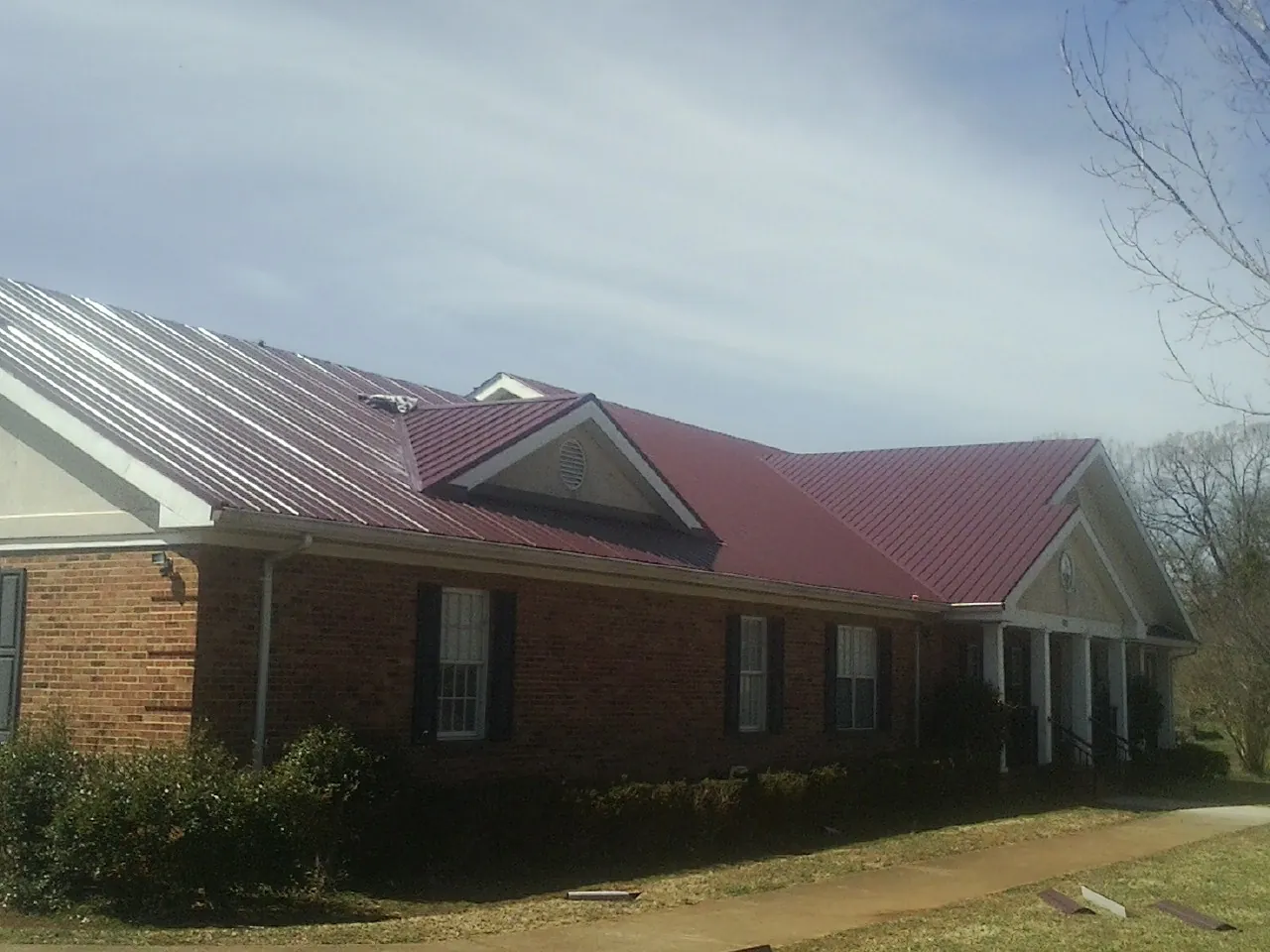 Red metal roof with gabled entries on a long brick building, from a Hail Damage Roof Repair job in North Ridgeville