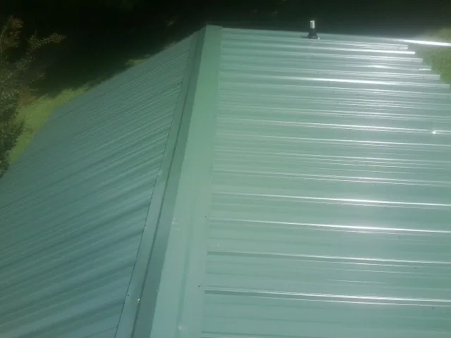 New green metal panels meeting at the ridge of a roof — Flat Roof Repair work by our crew in North Ridgeville