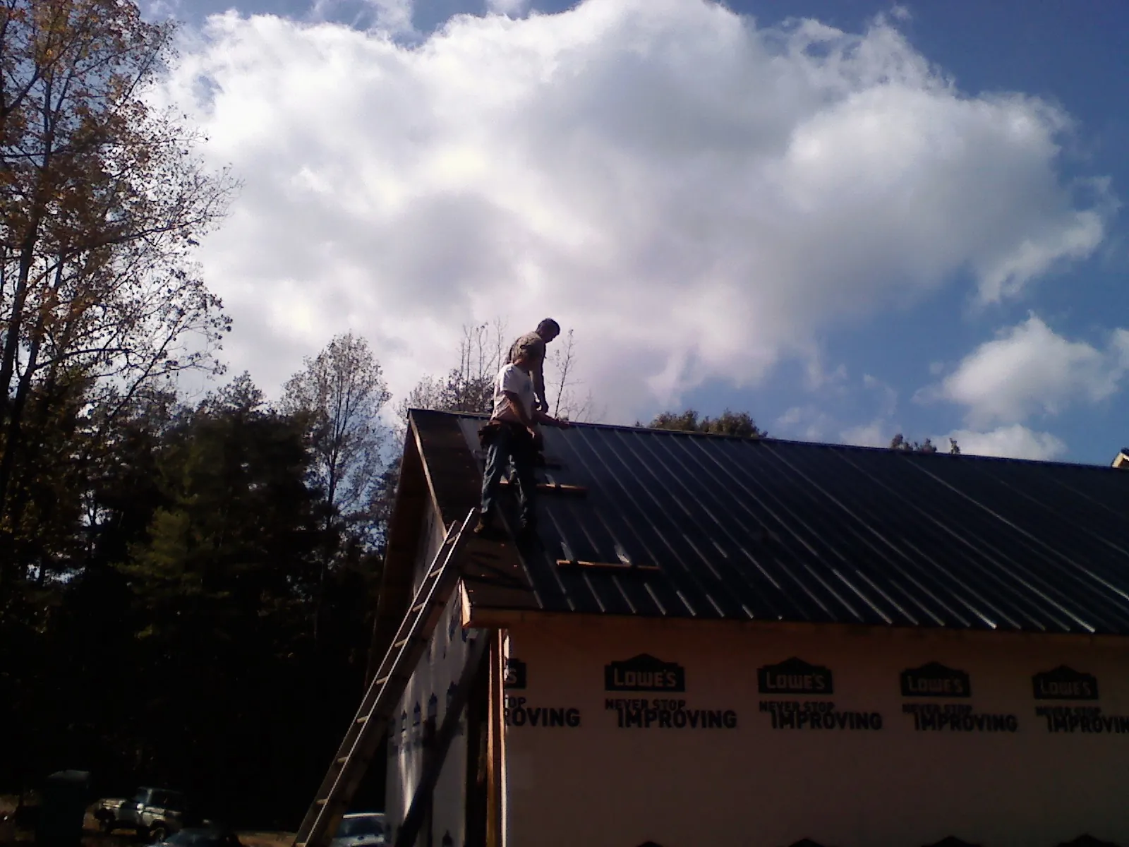 Roofer fastening dark metal panels high against a cloudy sky, from a Roof Inspection job in North Ridgeville