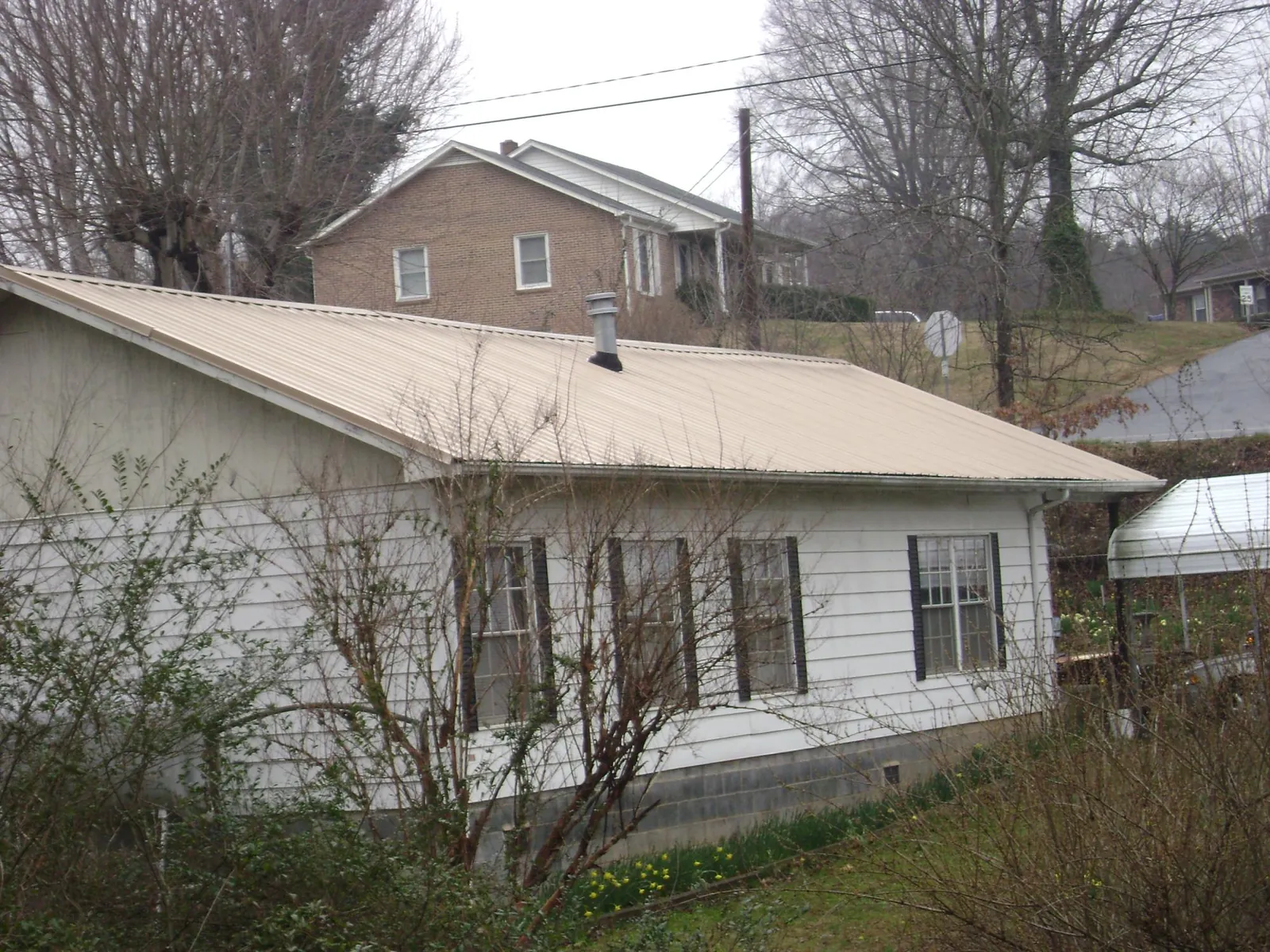 Tan metal roof on a white sided house set into a hillside — Commercial Roofing by Roofing Brothers in North Ridgeville